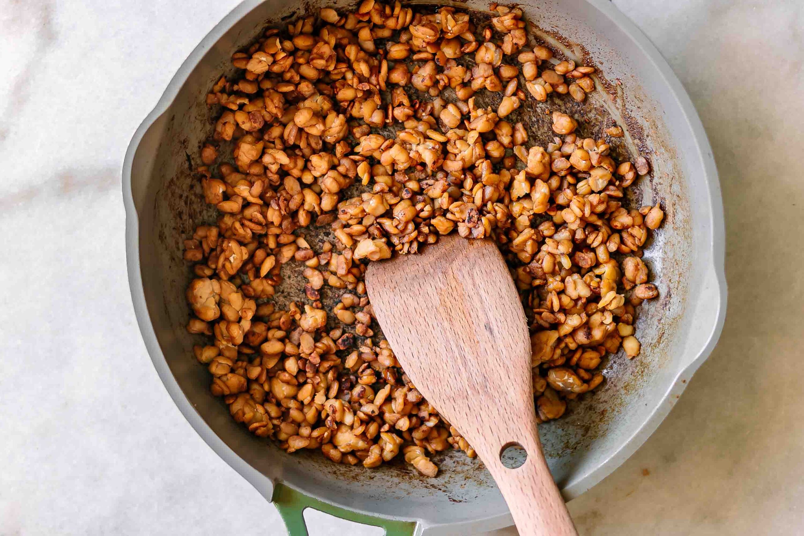 vegan bacon bits made of tempeh in a pan with a wooden spatula
