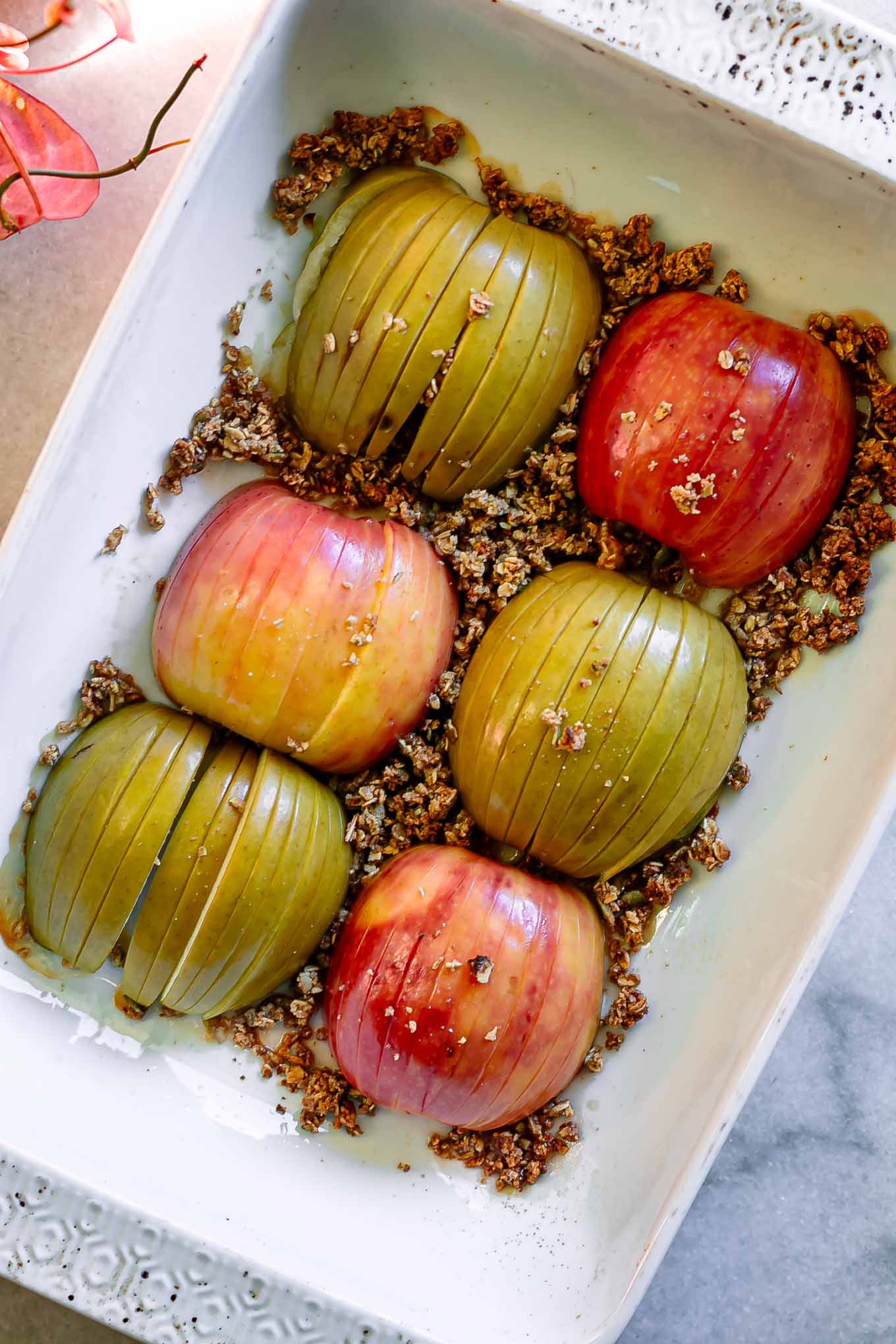 hasselback cut baked apples in a baking dish with granola