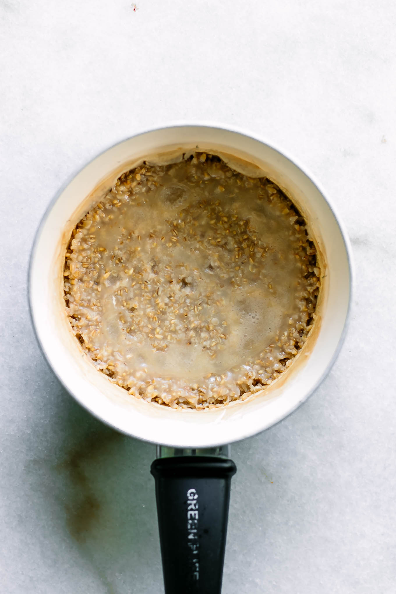 a small pot with steel but oats on a white table