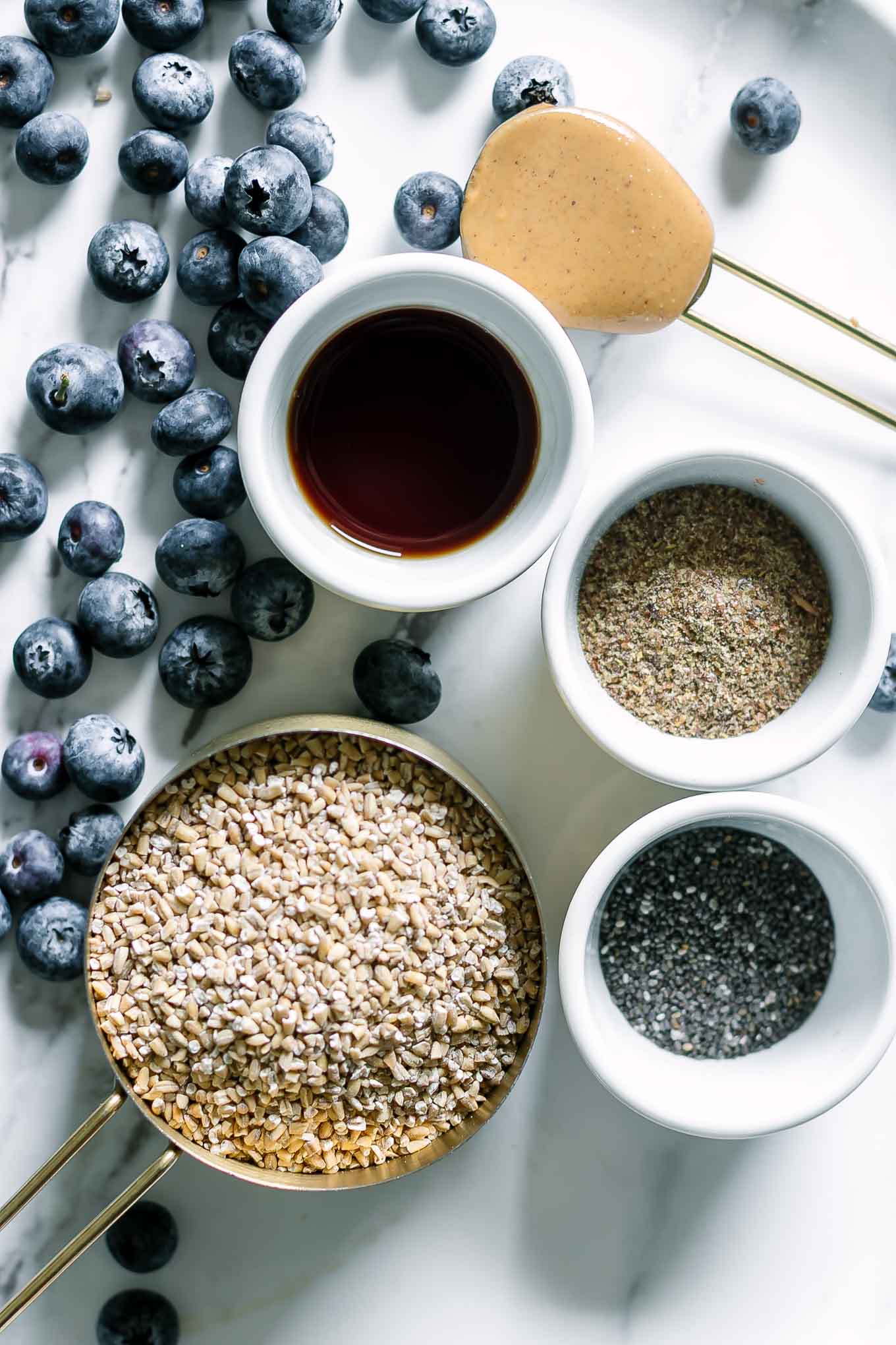 bowls of steel cut oats, vanilla, flax seeds, chia seeds, and nut butter on a table with fresh blueberries
