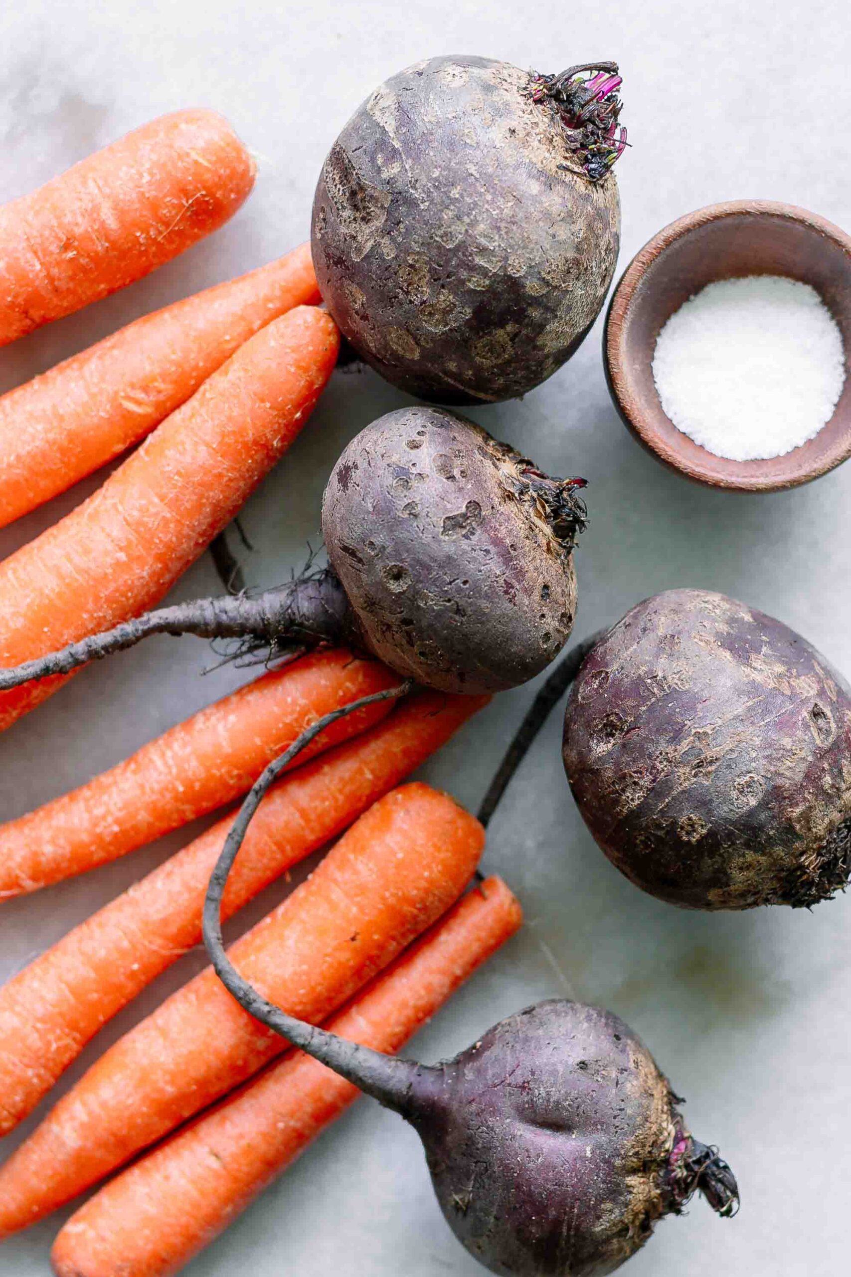 carrots and beets on a white table with a bowl of salt