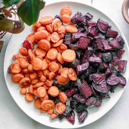 roasted beets and carrots on a white side dish serving plate on a white table with a bowl of salt
