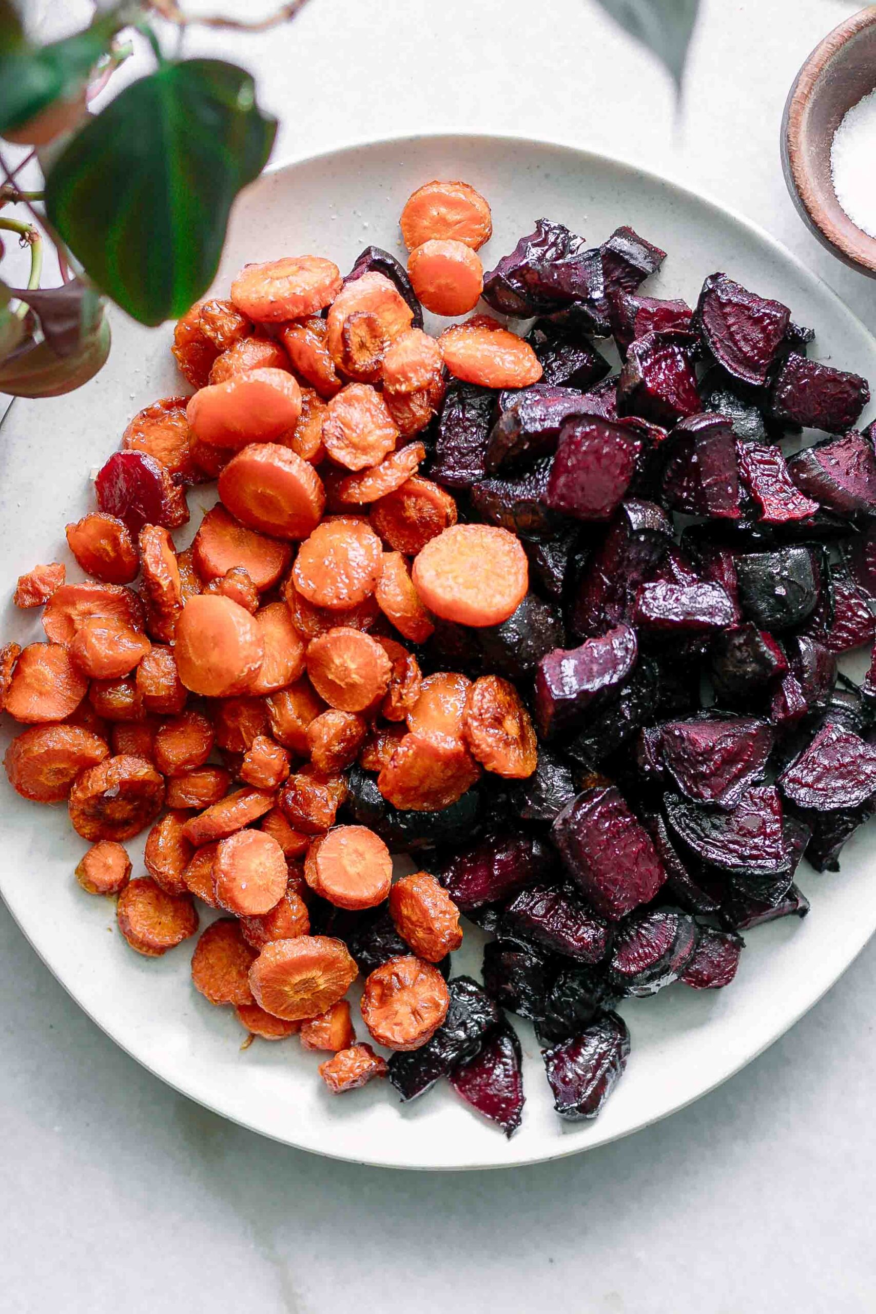 a close up of orange roasted carrots and red beets on a white serving plate